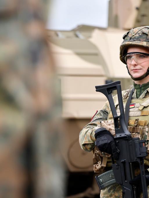 Eine Bundeswehr-Soldatin in Tarnanzug mit G36 Gewehr steht vor einem Militärfahrzeug