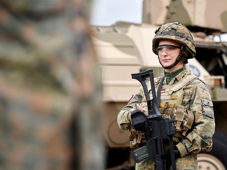 Eine Bundeswehr-Soldatin in Tarnanzug mit G36 Gewehr steht vor einem Militärfahrzeug