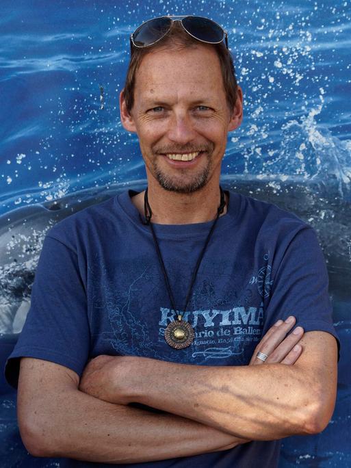 Fabian Ritter hält die Arme verschränkt und lächelt in die Kamera. Er trägt ein blaues T-Shirt und eine in die kurzen braunen Haare geschobene Sonnenbrille.