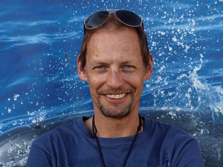 Fabian Ritter hält die Arme verschränkt und lächelt in die Kamera. Er trägt ein blaues T-Shirt und eine in die kurzen braunen Haare geschobene Sonnenbrille.