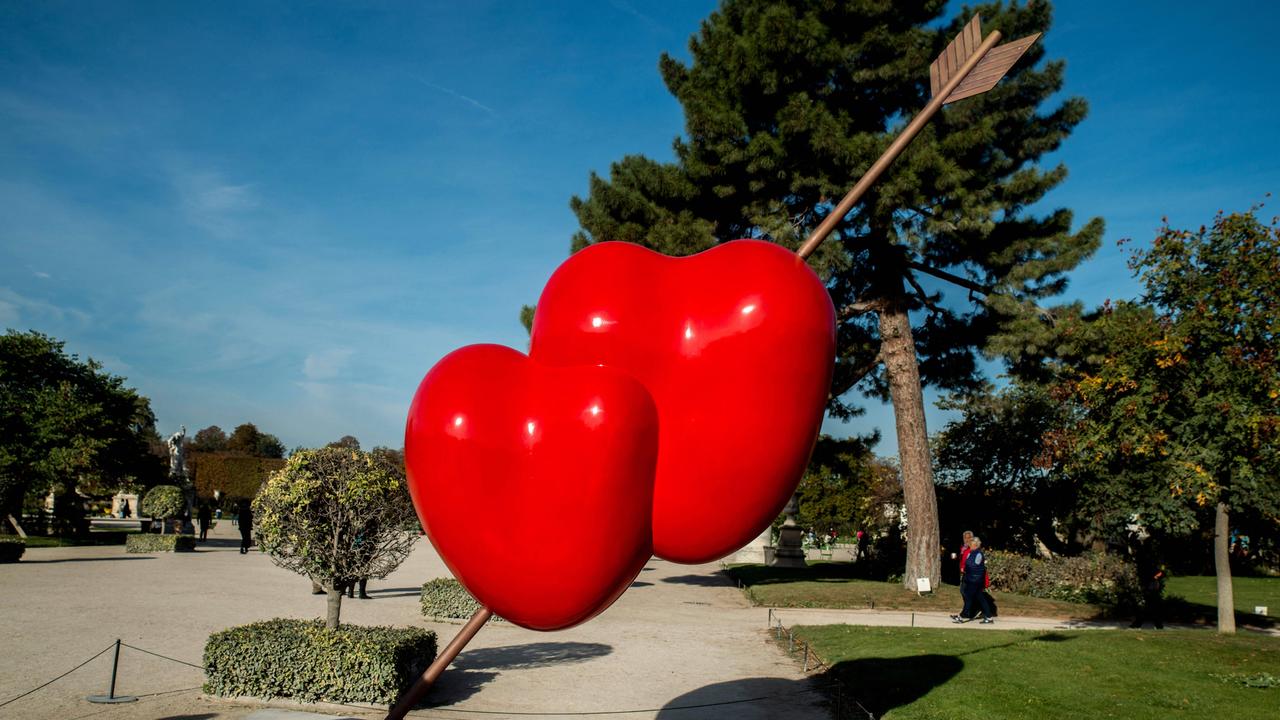 Gaetano Pesces Skulptur "Double Heart": Zwei rote Herzen sind von einem Pfeil durchbohrt. Dahinter stehen Bäume.
