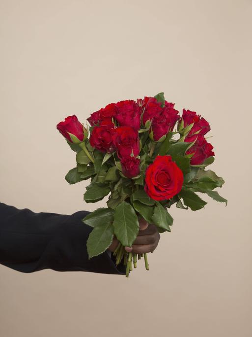 Eine ausgestreckte Hand hält einen Strauß rote Rosen.