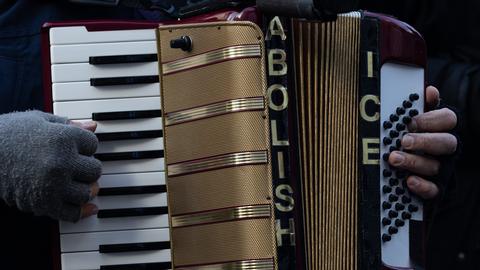 Bei einer Protestkundgebung hält ein Mensch ein Akkordion. Darauf steht geschrieben: Abolish ICE - eine Forderung, die US-Einwanderungsbehörde ICE zu schließen. Bei einer Protestkundgebung hält ein Mensch ein Akkordion. Darauf steht geschrieben: Abolish ICE - eine Forderung, die US-Einwanderungsbehörde ICE zu schließen.