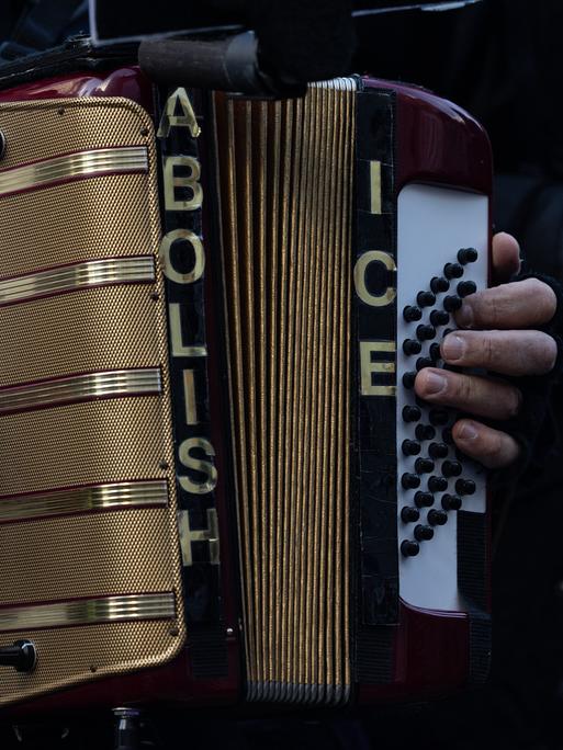 Bei einer Protestkundgebung hält ein Mensch ein Akkordion. Darauf steht geschrieben: Abolish ICE - eine Forderung, die US-Einwanderungsbehörde ICE zu schließen.