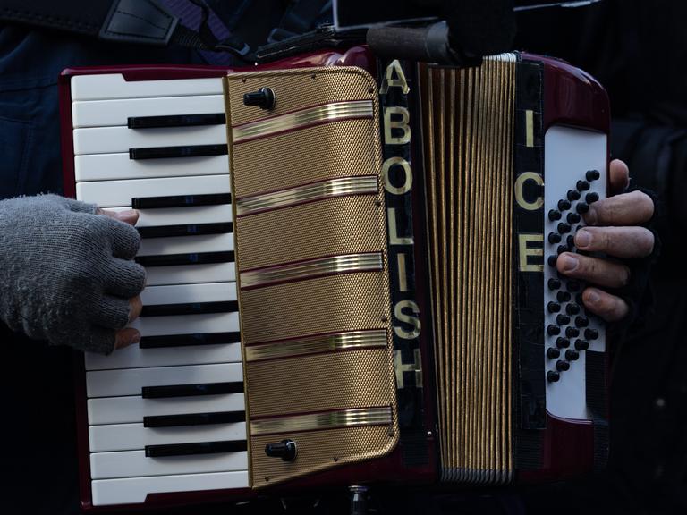 Bei einer Protestkundgebung hält ein Mensch ein Akkordion. Darauf steht geschrieben: Abolish ICE - eine Forderung, die US-Einwanderungsbehörde ICE zu schließen.