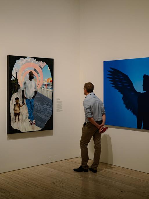 Ein Mann in einer Kunstgalerie betrachtet nachdenklich großformatige Gemälde.