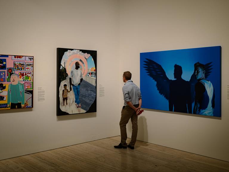Ein Mann in einer Kunstgalerie betrachtet nachdenklich großformatige Gemälde.