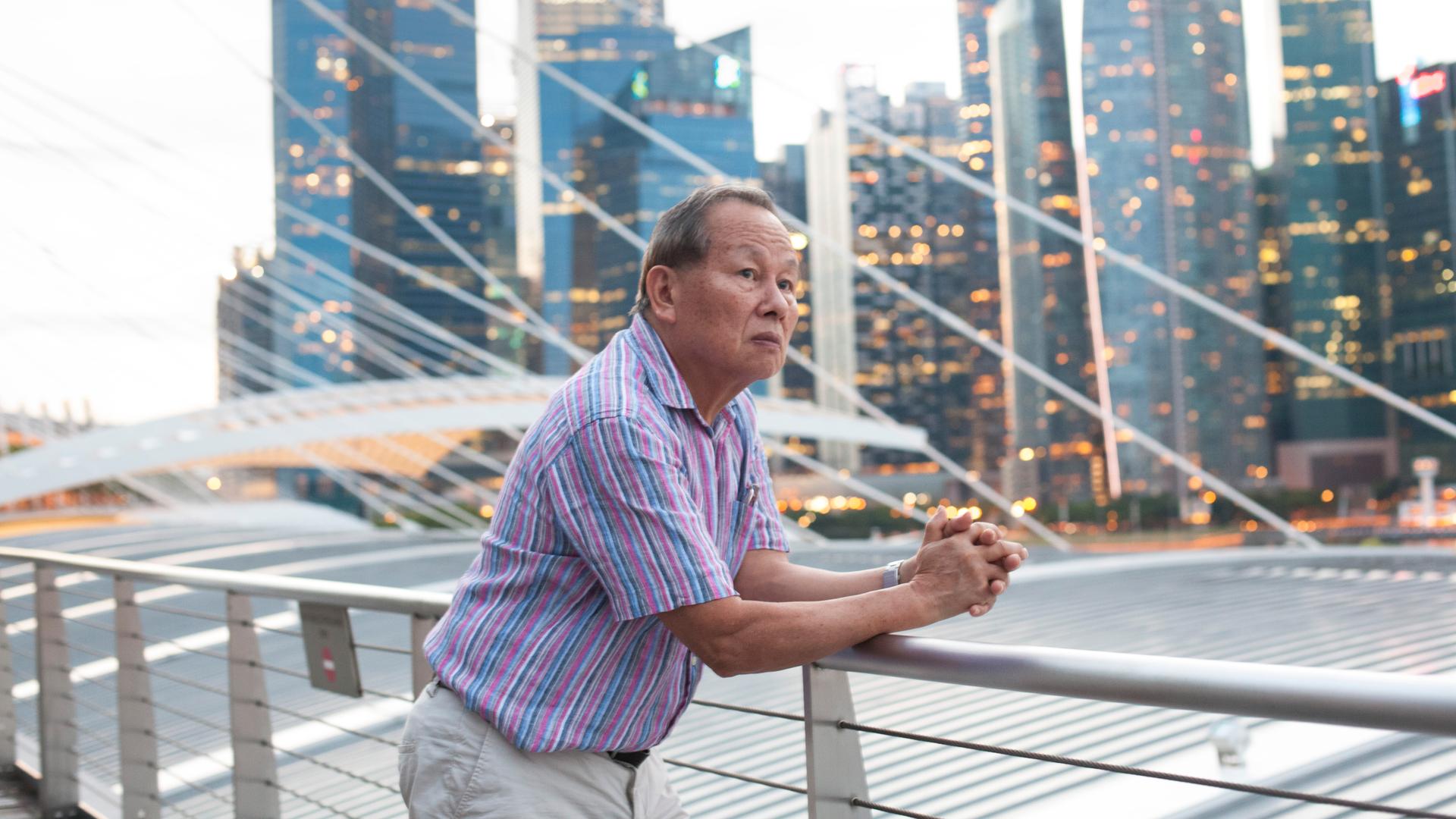 Singapur – Asiatisches Porträt: Ein älterer Mann blickt auf die modern Hochhauslandschaft in Singapur und denkt über die Zukunft nach