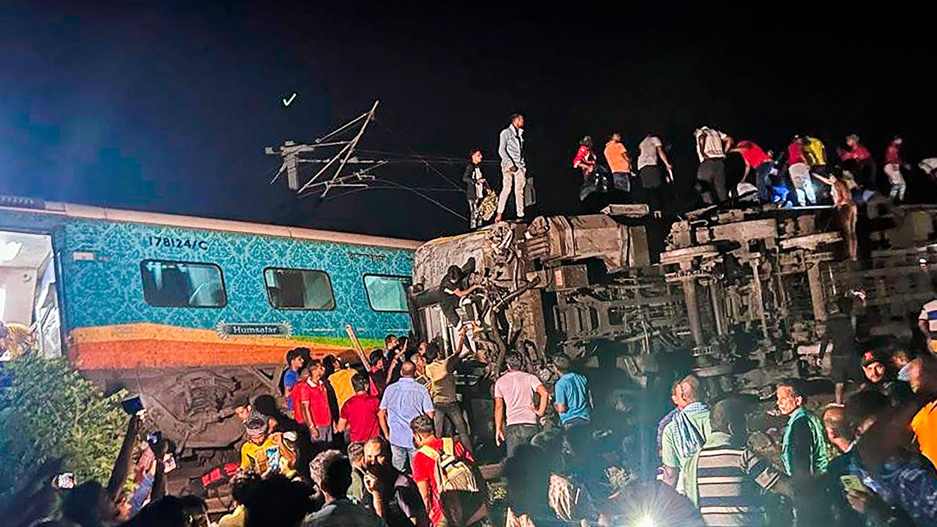 Mehrere Menschen stehen auf und neben einem entgleisten Zugwaggon im Osten Indiens.