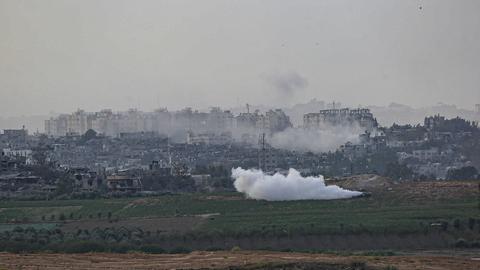 Israelische Panzer fahren über ein Feld und ziehen eine dicke Rauchwolke hinter sich her, im Hintergrund Häuser im Gazastreifen mit aufsteigendem Qualm.