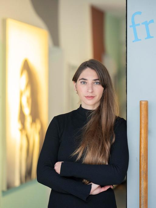 Deborah Schnabel steht am Eingang zu einem Ausstellungsraum, im Hintergrund ist ein Porträt von Anne Frank zu sehen.