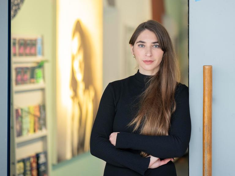 Deborah Schnabel steht am Eingang zu einem Ausstellungsraum, im Hintergrund ist ein Porträt von Anne Frank zu sehen.