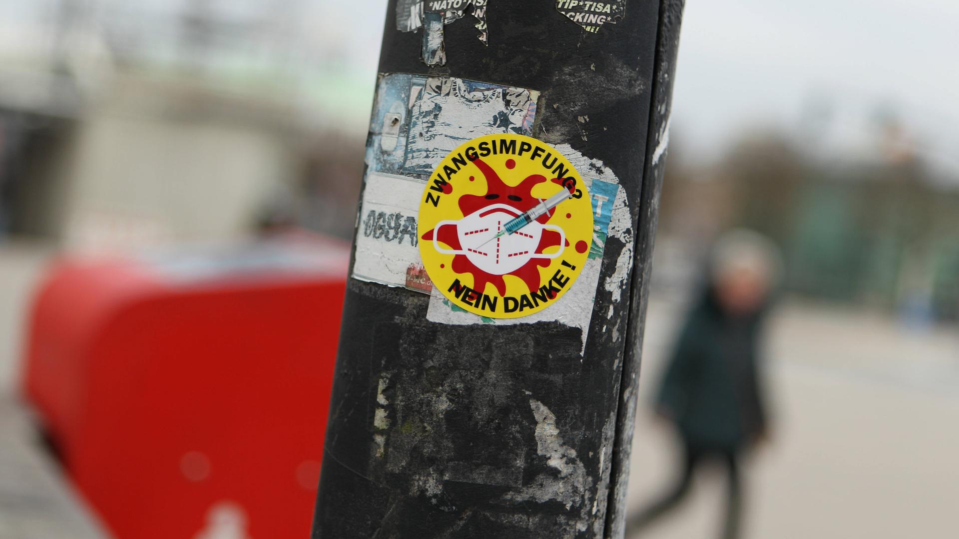 Sticker an einem Laternenpfahl, auf dem steht "Zwangs-Impfung? Nein danke". Das Motiv, ein rotes Coronavirus auf gelben Grund, erinnert an die Anti-Atomkraft-Aufkleber mit dem Text "Atomkraft? Nein danke".