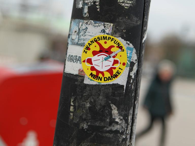 Sticker an einem Laternenpfahl, auf dem steht "Zwangs-Impfung? Nein danke". Das Motiv, ein rotes Coronavirus auf gelben Grund, erinnert an die Anti-Atomkraft-Aufkleber mit dem Text "Atomkraft? Nein danke".