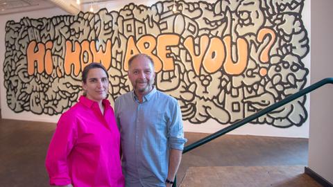 Anna Wagner und Marcus Droß, das neue Leitungsteam des Künstlerhauses Mousonturm, nach dem Pressegespräch zu ihrer neuen Aufgabe. Im Hintergrund ein Graffito mit dem Schriftzug "Hi, how are you". 