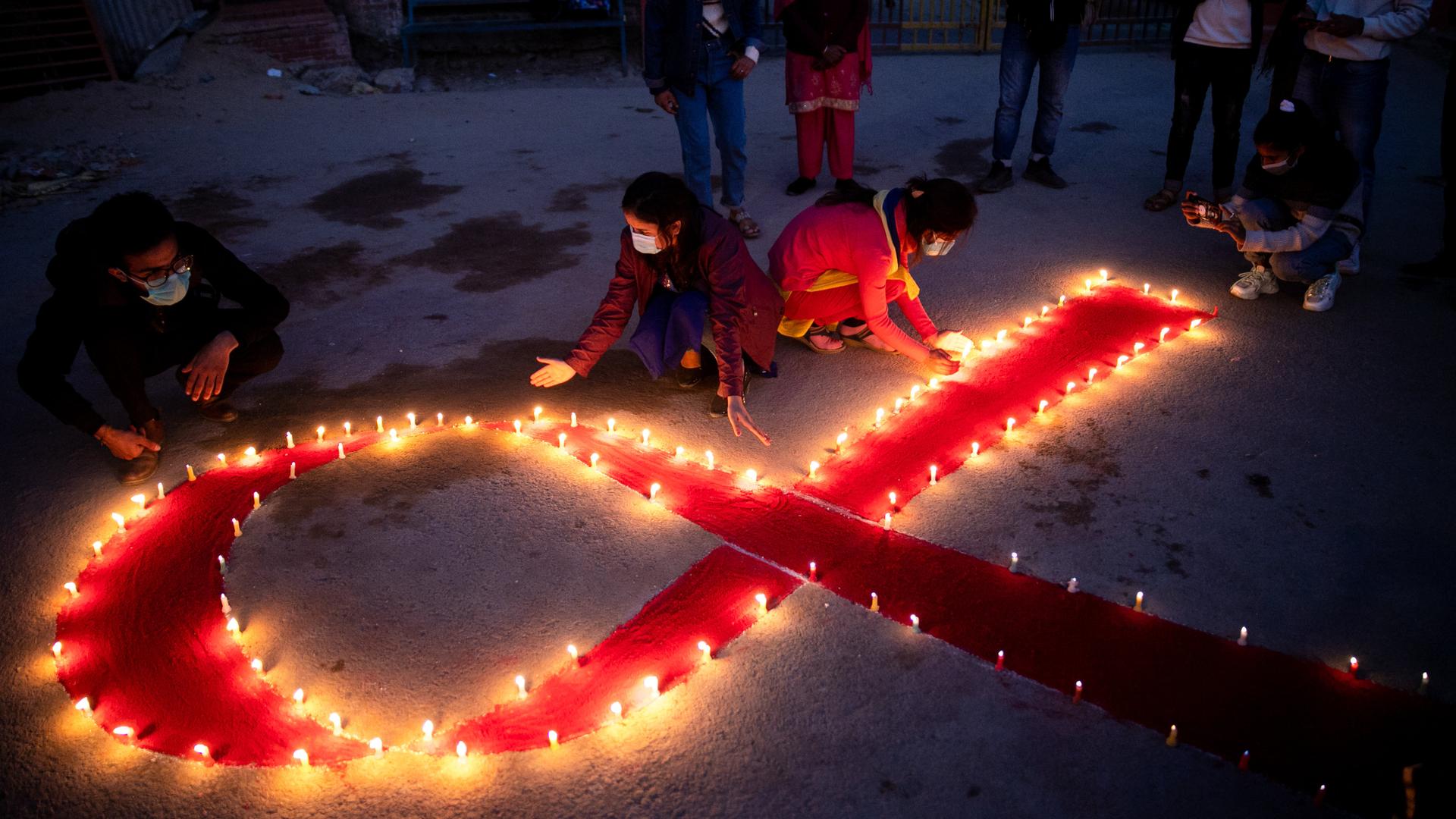 Mädchen und Frauen in Nepal haben das Symbol zum Bewusstsein von Aids - eine rote Schleife - mit Kerzen auf dem Boden nachgebildet.