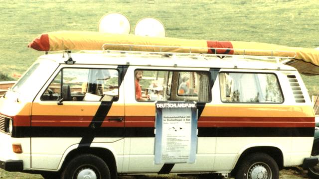 Ein VW-Bus mit einem aufgeklebten Deutschlandfunk-Plakat steht auf einer Wiese in Elspe, 1981
