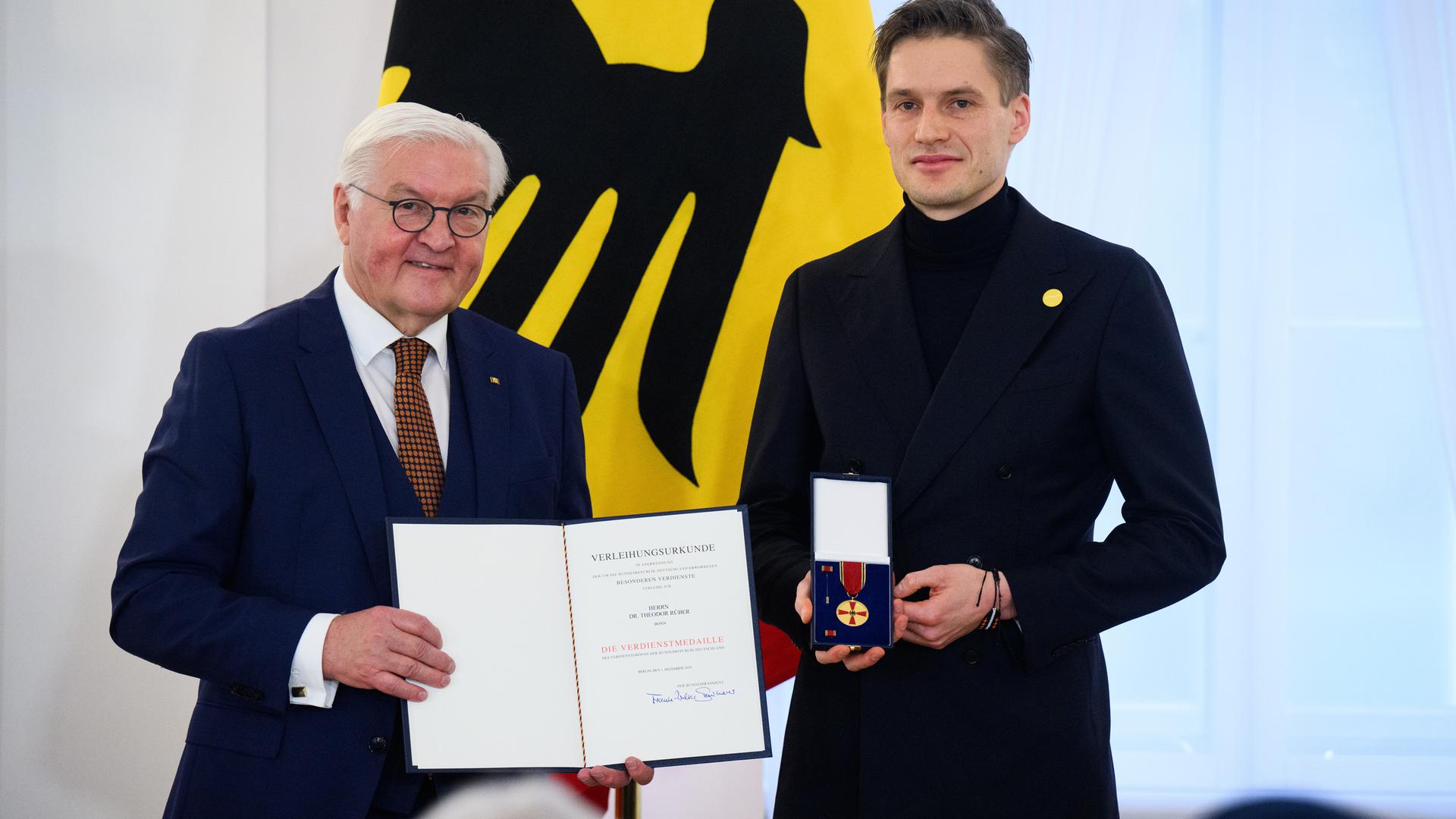 Theodor Rüber steht neben Bundespräsident Frank-Walter Steinmeier. Rüber hält die Bundesverdienstmedaille in den Händen, Steinmeier die dazugehörige Urkunde.