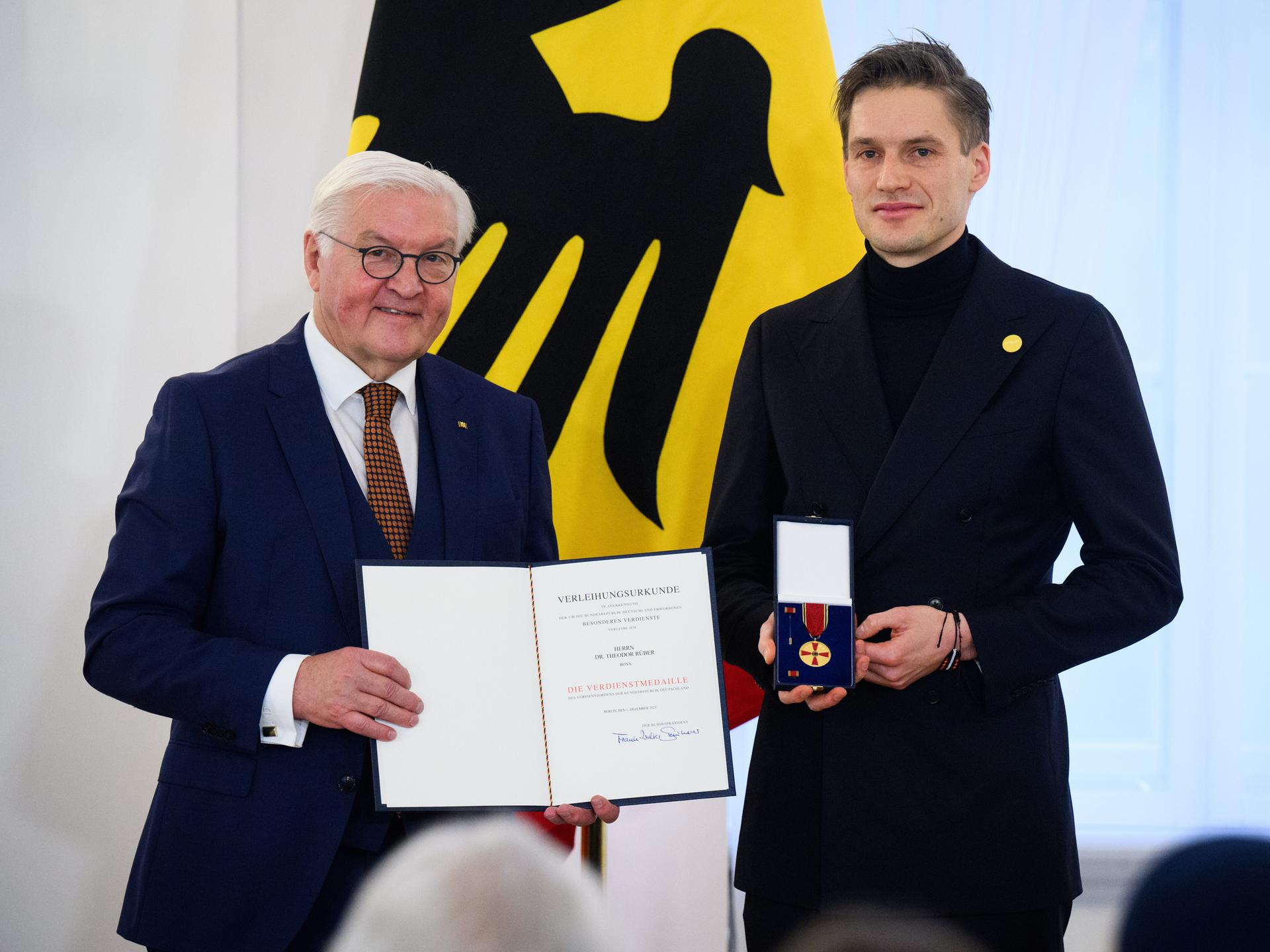 Theodor Rüber steht neben Bundespräsident Frank-Walter Steinmeier. Rüber hält die Bundesverdienstmedaille in den Händen, Steinmeier die dazugehörige Urkunde.