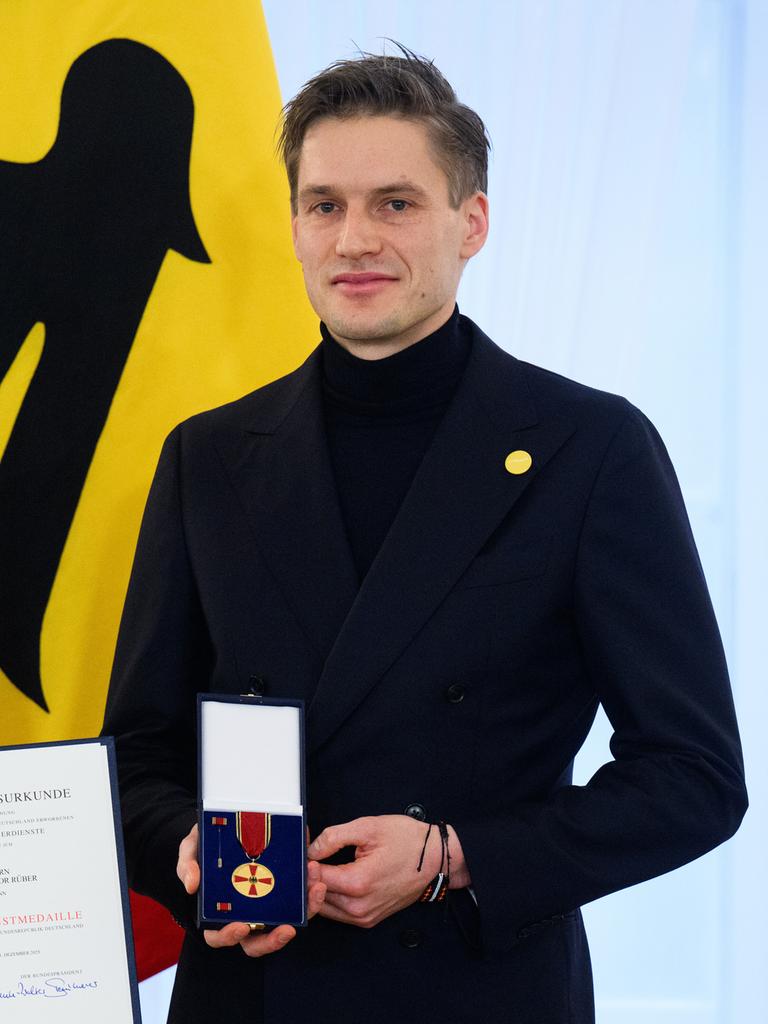 Theodor Rüber steht neben Bundespräsident Frank-Walter Steinmeier. Rüber hält die Bundesverdienstmedaille in den Händen, Steinmeier die dazugehörige Urkunde.