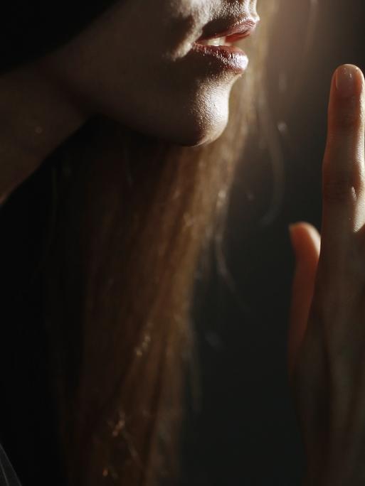 Eine Frau deutet mit dem Finger vor dem Mund ein Geheimnis an.