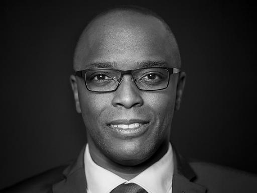 Frontales schwarz-weiß Porträt von Thomas Kapapa, der freundlich in die Kamera schaut.