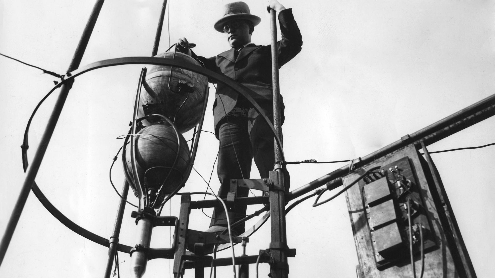 Ein Schwarz-Weiß-Foto zeigt Johannes Winkler mit einem Raketenmotor in einem gerüstartigen Aufbau auf einem Raketentestgelände bei Berlin. Ein Schwarz-Weiß-Foto zeigt Johannes Winkler mit einem Raketenmotor in einem gerüstartigen Aufbau auf einem Raketentestgelände bei Berlin.
