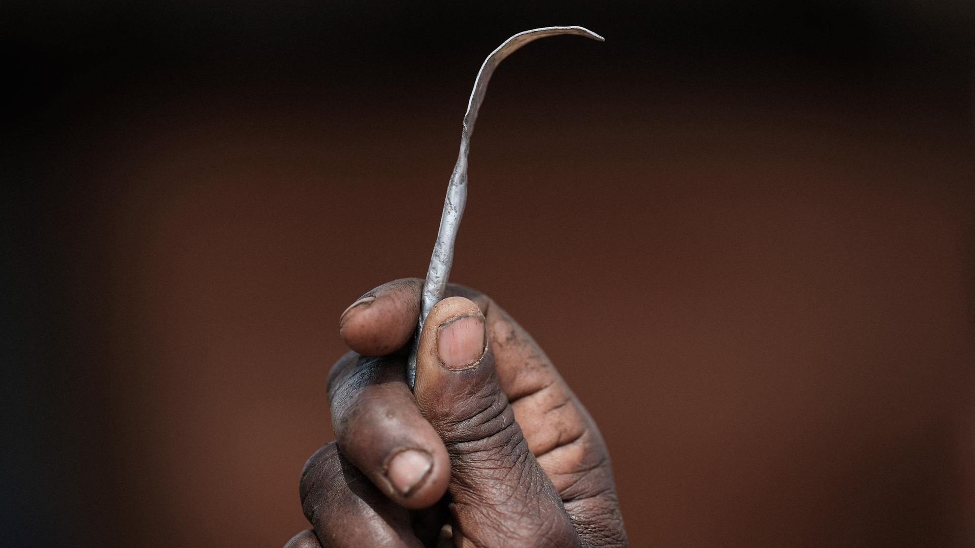 Nahaufnahme einer Hand, die ein selbstgemachtes Instrument aus einem platt gebogenen Metallnagel hängt. Nahaufnahme einer Hand, die ein selbstgemachtes Instrument aus einem platt gebogenen Metallnagel hängt.