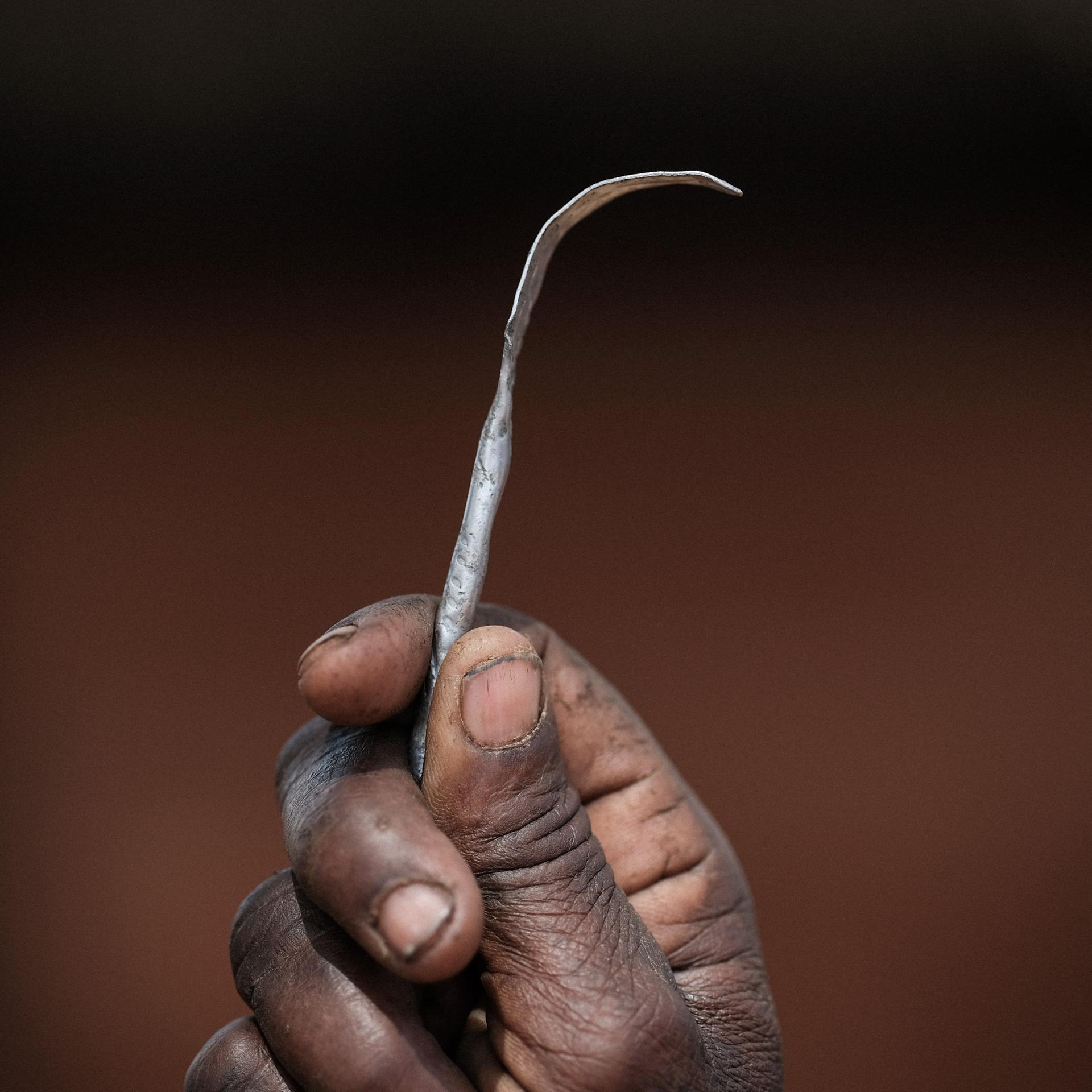 Nahaufnahme einer Hand, die ein selbstgemachtes Instrument aus einem platt gebogenen Metallnagel hängt.