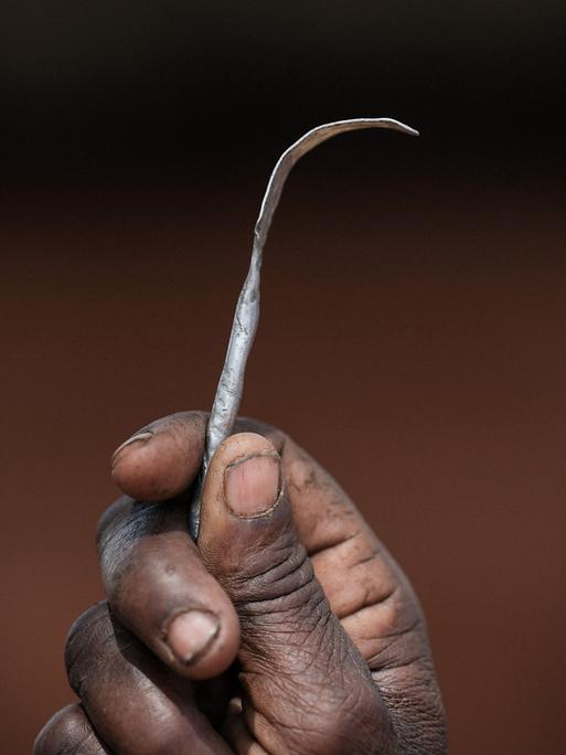 Nahaufnahme einer Hand, die ein selbstgemachtes Instrument aus einem platt gebogenen Metallnagel hängt.