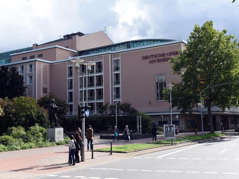 Das Opernhaus in Düsseldorf- ein großes ockerfarbenes Gebäude. Daneben ist eine Straße. Im Vordergund sind Passanten zu sehen. 
