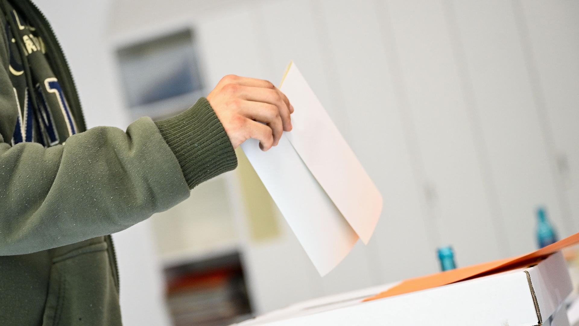 Ein Stimmzettel wird in die Urne geworfen.