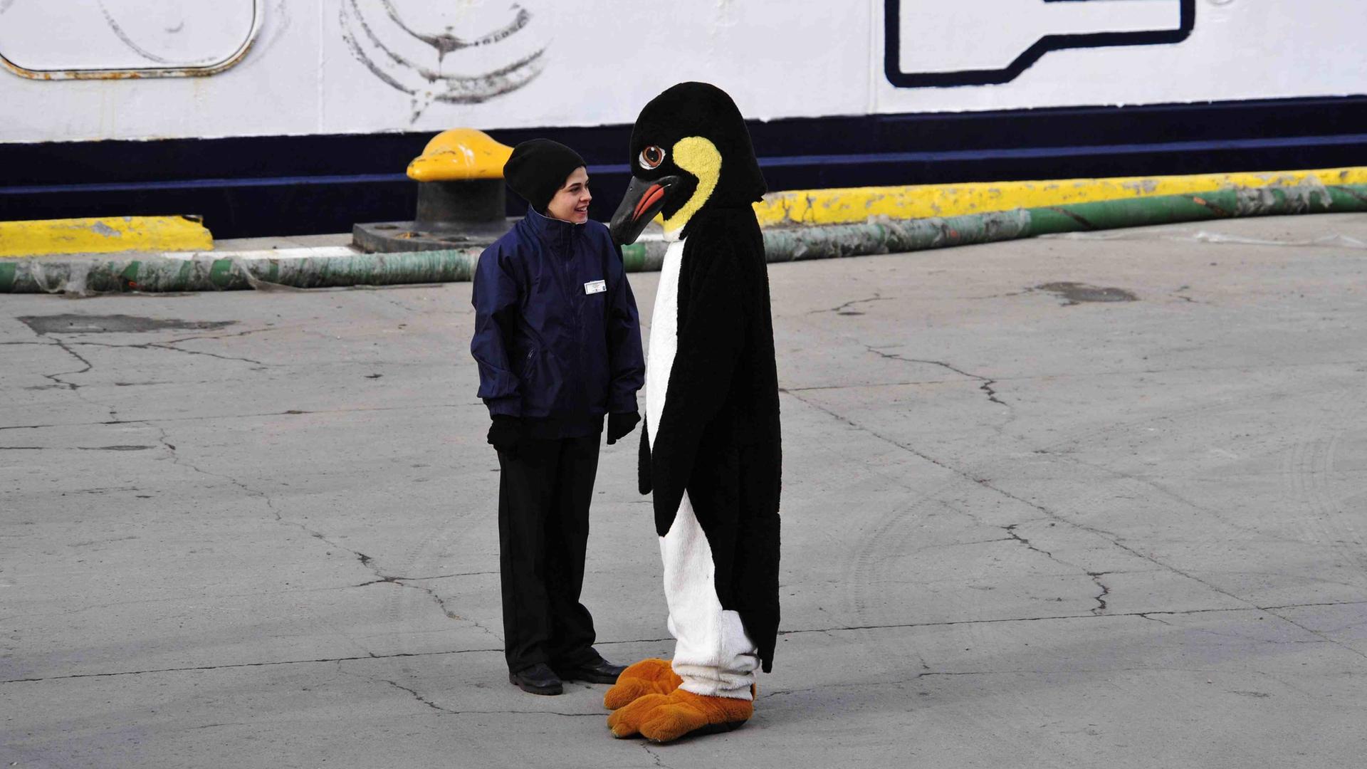 Ein älteres Kind steht einer Person in Pinguinkostüm gegenüber