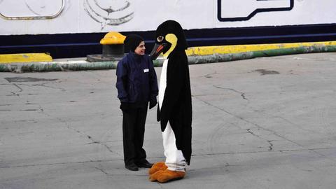 Ein älteres Kind steht einer Person in Pinguinkostüm gegenüber