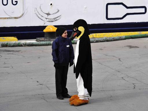 Ein älteres Kind steht einer Person in Pinguinkostüm gegenüber Ein älteres Kind steht einer Person in Pinguinkostüm gegenüber