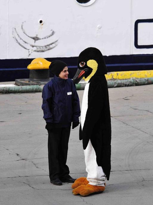 Ein älteres Kind steht einer Person in Pinguinkostüm gegenüber