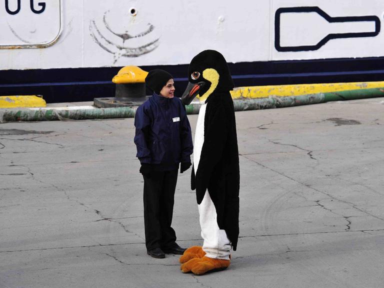 Ein älteres Kind steht einer Person in Pinguinkostüm gegenüber Ein älteres Kind steht einer Person in Pinguinkostüm gegenüber