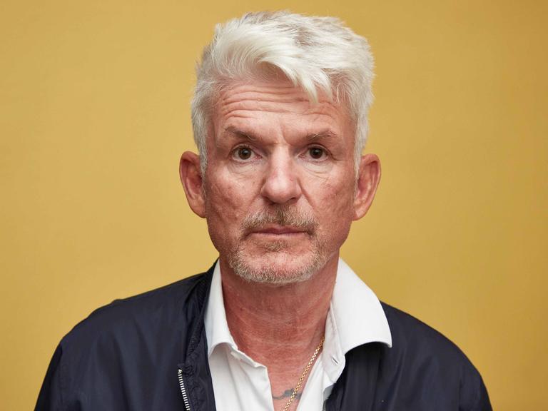 Porträt von Heinz Strunk vor einer gelben Wand.