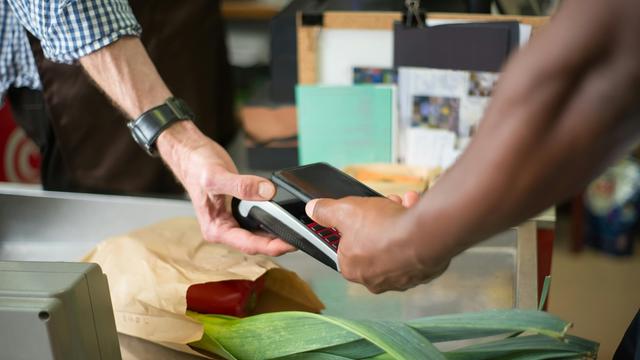 Eine Person bezahlt Lebensmittel, indem sie das Handy auf ein Kartenterminal legt.