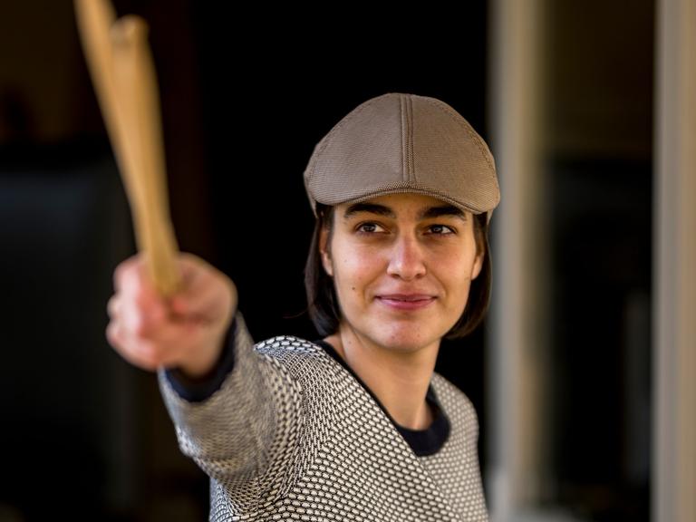 Leonie Klein mit Mütze lächelt in die Kamera, während sie zwei Schlegel mit ihrer rechten Hand nach vorn streckt.