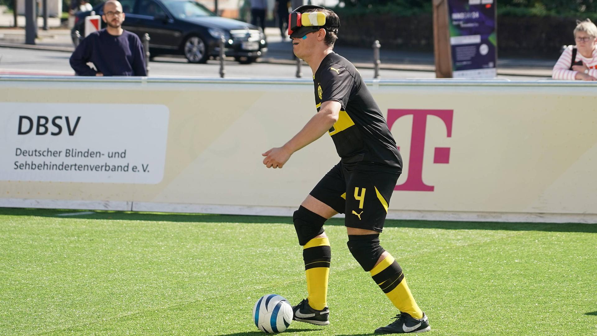 Ein Mann in Sportkleidung spielt einen Fußball. Er trägt eine Art Verdunklungsbrille.