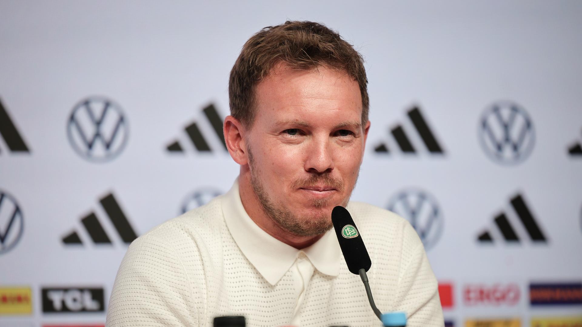 Nagelsmann sitzt an einem Tisch und spricht in ein Mikrofon. Dahinter eine weiße Wand mit schwarzen Logos der Sponsoren