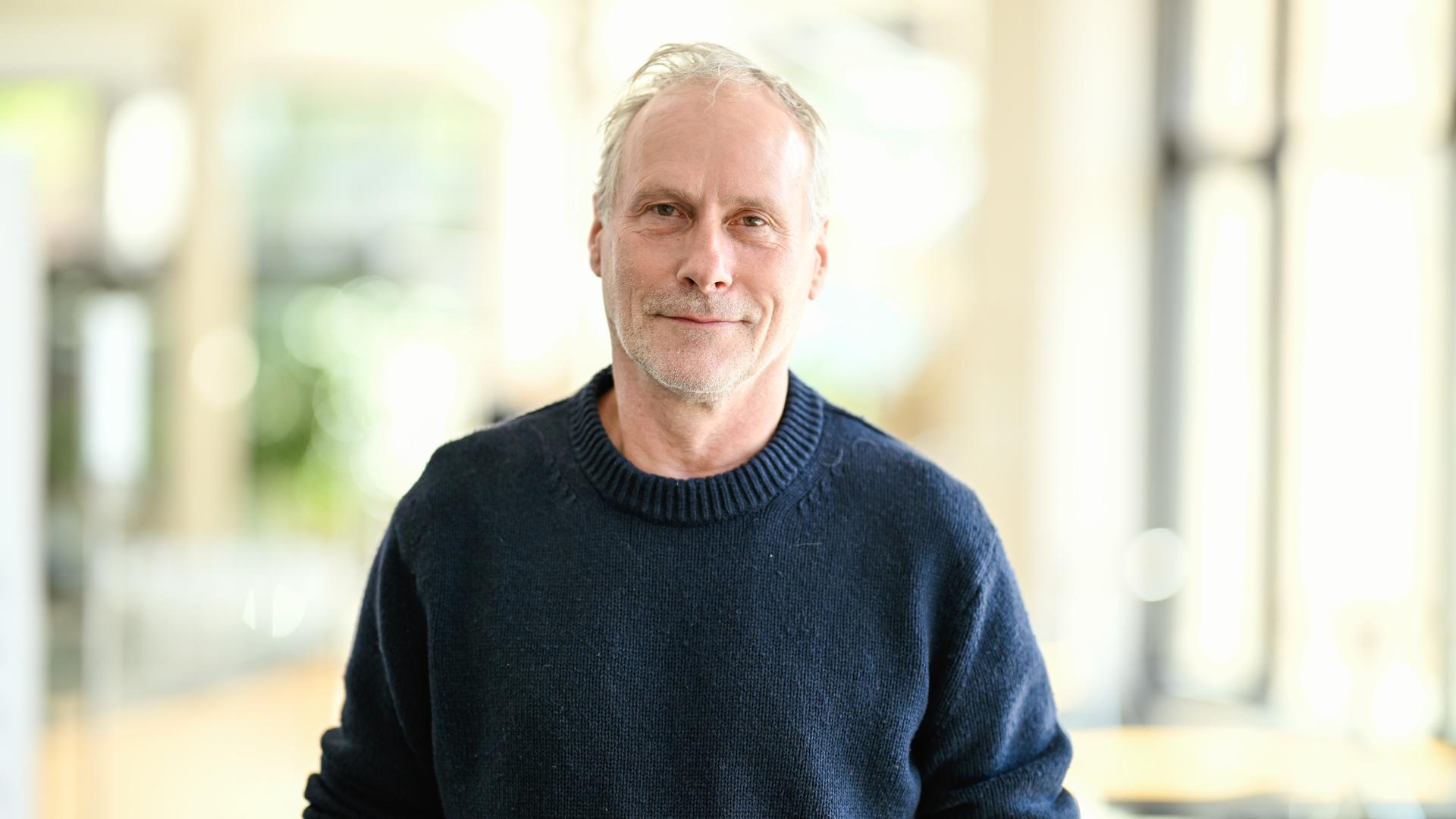 Der Schauspieler Wolfram Koch steht vor einer Pressekonferenz zum neuen Stück der Nibelungen-Festspiele. Er trägt einen dunkelblauen Pullover und schaut freundlich in die Kamera. Der Schauspieler Wolfram Koch steht vor einer Pressekonferenz zum neuen Stück der Nibelungen-Festspiele. Er trägt einen dunkelblauen Pullover und schaut freundlich in die Kamera.