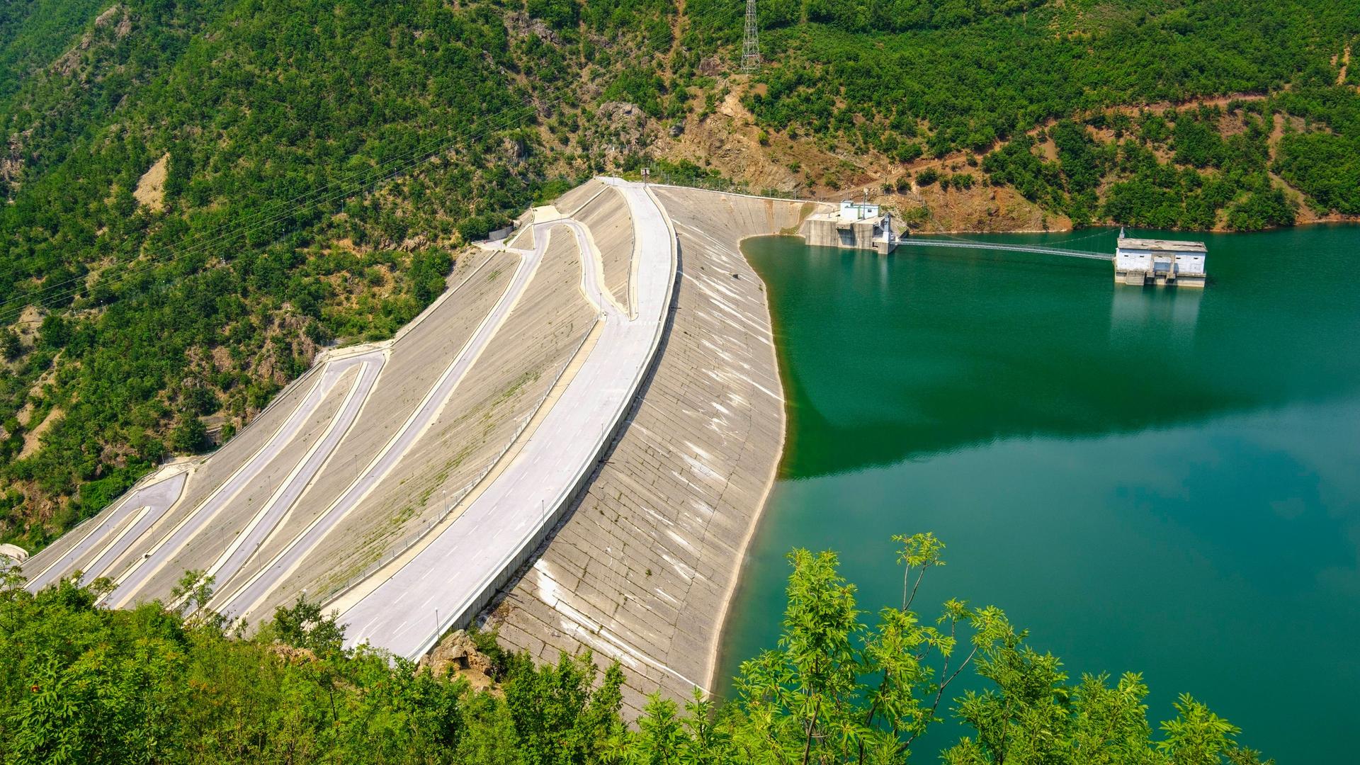Der Fierza-Stausee ist mit seiner Fläche von 72,6 Quadratkilometern der größte Stausee in Albanien. Grünblaues Wasser wird von einer Staumauer gehalten, die weit in die Tiefe ragt.