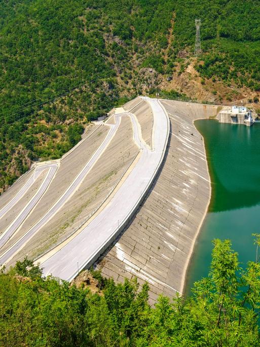 Der Fierza-Stausee ist mit seiner Fläche von 72,6 Quadratkilometern der größte Stausee in Albanien. Grünblaues Wasser wird von einer Staumauer gehalten, die weit in die Tiefe ragt.