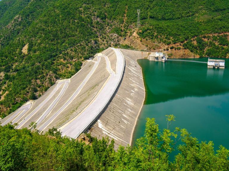 Der Fierza-Stausee ist mit seiner Fläche von 72,6 Quadratkilometern der größte Stausee in Albanien. Grünblaues Wasser wird von einer Staumauer gehalten, die weit in die Tiefe ragt.