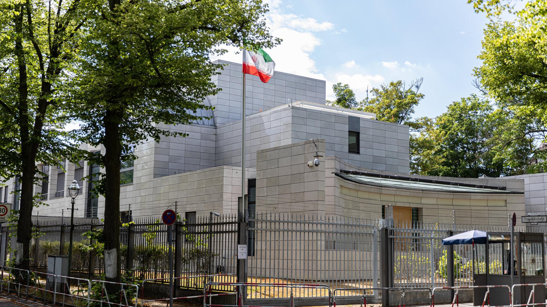 Das Foto zeigt die iranische Botschaft in Berlin. Vor dem grauen Gebäude steht ein hoher Zaun. Auf dem Gelände weht die iranische Fahne.