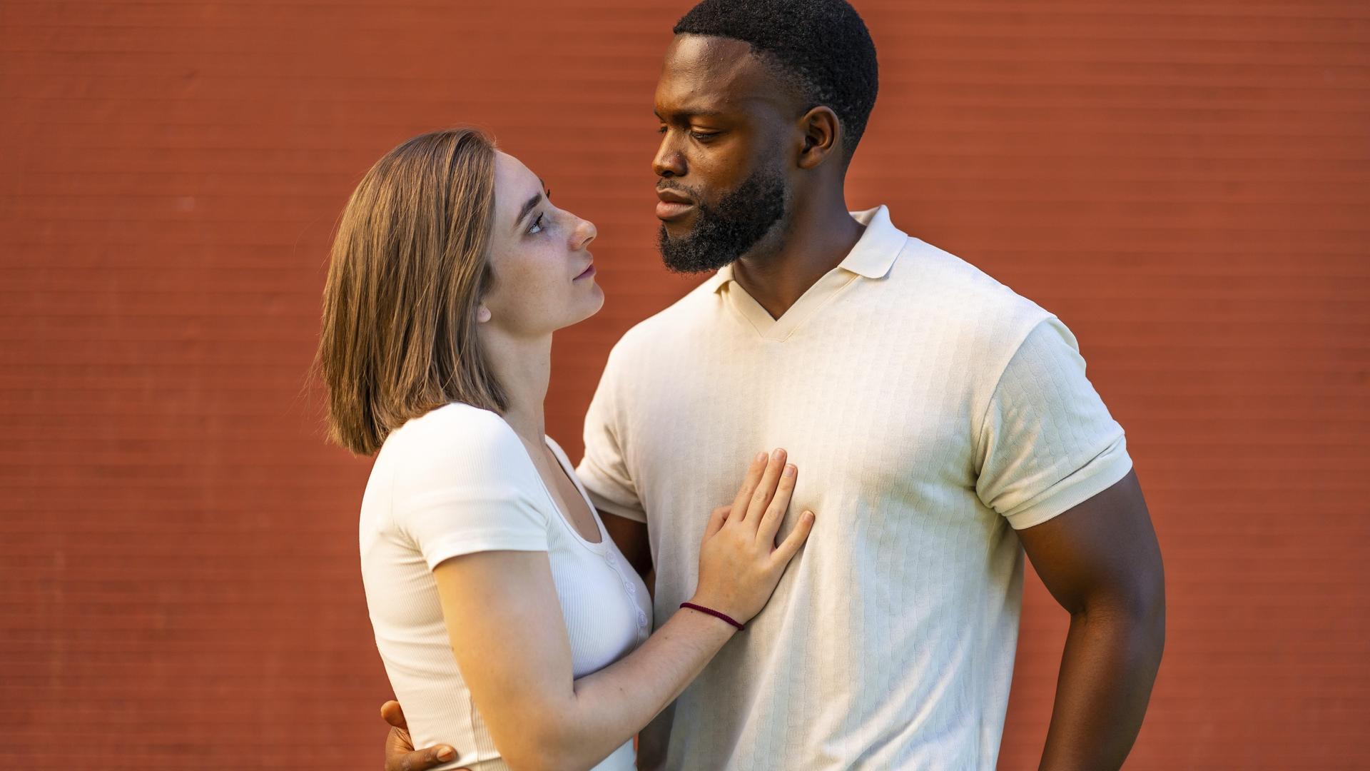 Ein Paar, das sich umarmend vor einer roten Backsteinmauer steht und sich ansieht