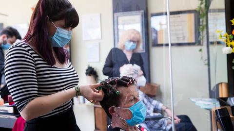 Eine Friseurin in einem Friseursalon nimmt einer Kundin Lockenwickel aus den Haaren.