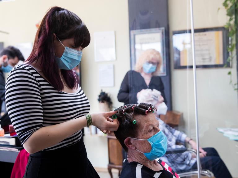 Eine Friseurin in einem Friseursalon nimmt einer Kundin Lockenwickel aus den Haaren.